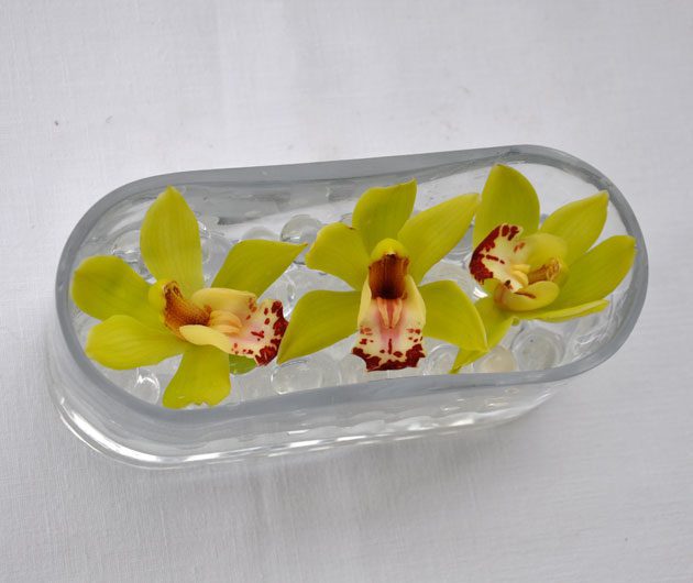 Three yellow orchids on ice in glass dish