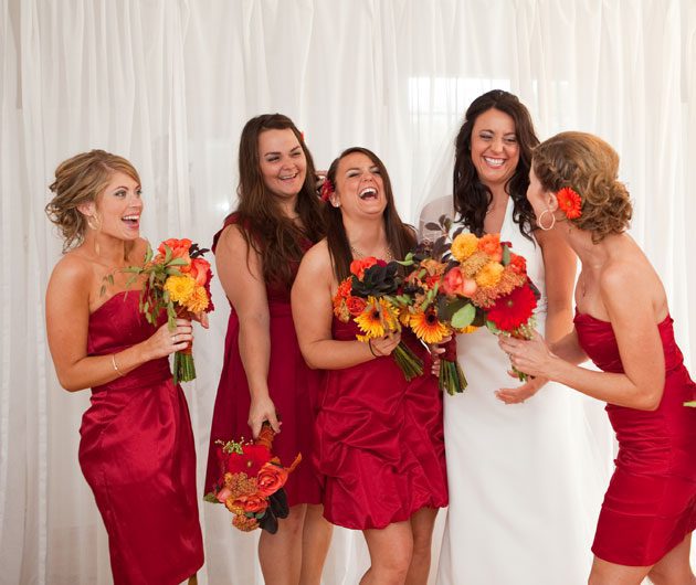 Bride laughing with bridesmaids in red dresses
