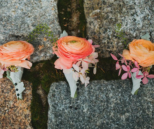 Three peach ranunculus boutonnieres on mossy stones